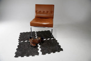 Hier ist ein Stuhl mit 4 losen PVC Bodenplatten und einem Paar Schuhen darunter zu sehen.