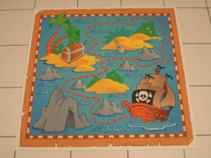 Auf diesem Bild ist eine kleine Spielfläche für Kinder zu sehen. Ein Piratenschiff und Inseln sind auf PVC Bodenfliesen aufgedruckt.